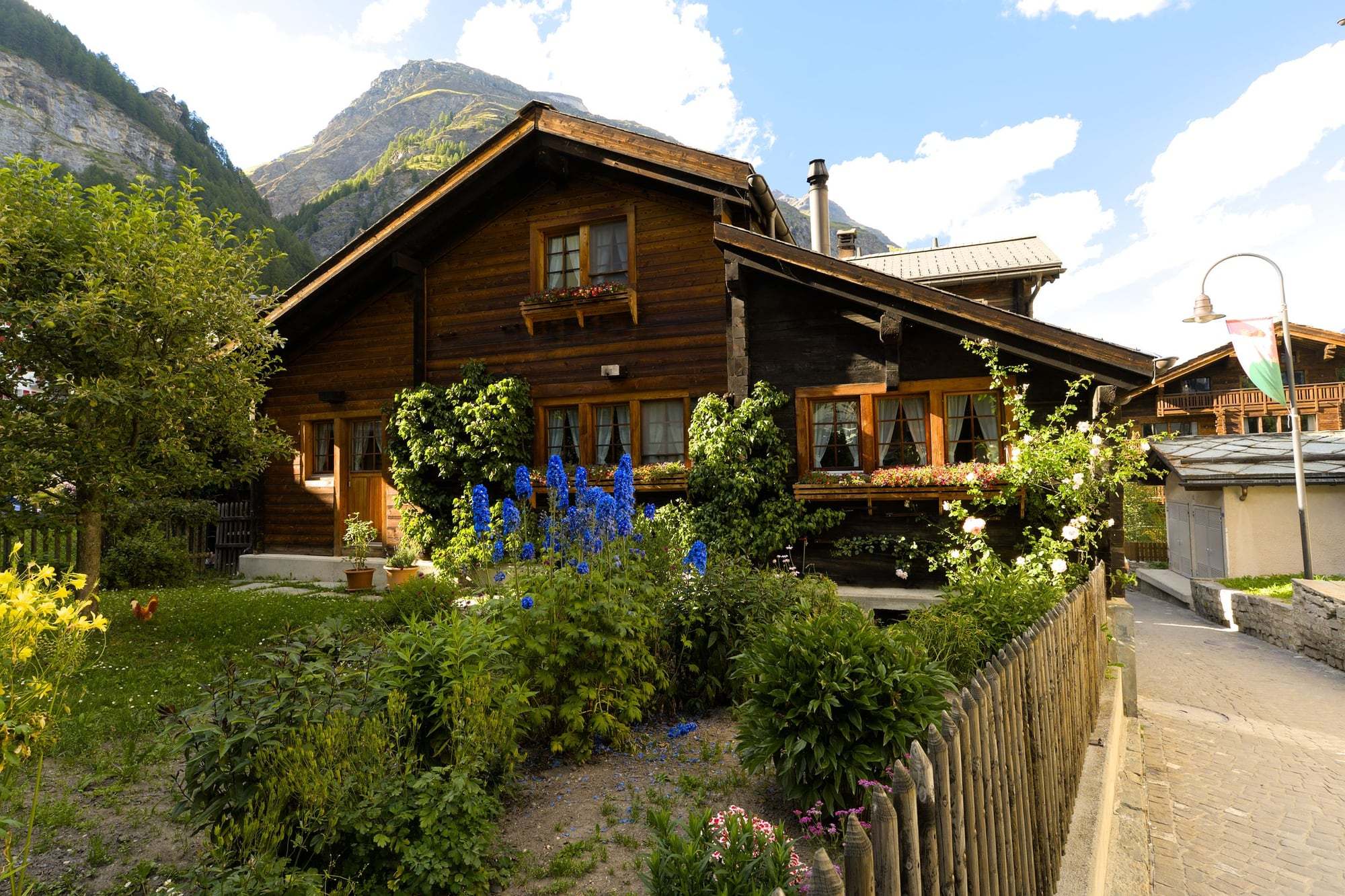 Chalet en bois foncé avec jardin fleuri devant des montagnes